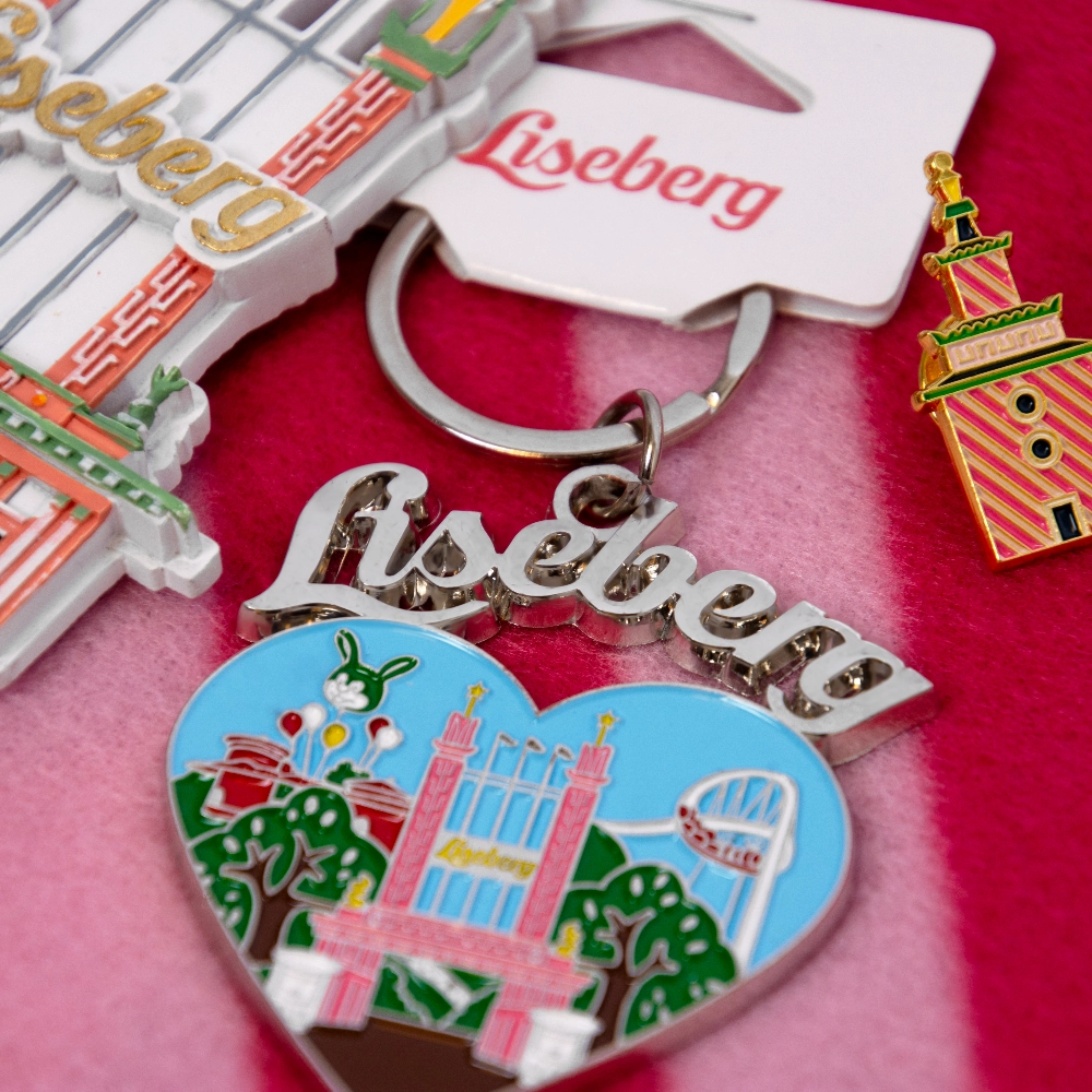 F&auml;rgglada Liseberg-souvenirer, inklusive nyckelringar och ett hj&auml;rtformat m&auml;rke, ligger samlade p&aring; ett rosa tyg.