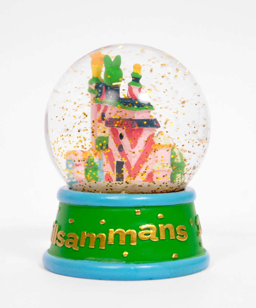 En n&auml;rbild av en Liseberg-sn&ouml;glob som visar ett miniatyrhus i rosa och gr&ouml;nt, med guldglitter som sv&auml;var i globen. Den gr&ouml;na basen har en bl&aring; kant och ordet "tillsammans" i guldtext.
